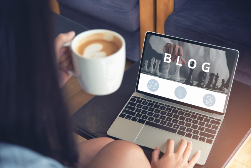 Over-shoulder view of a person holding a mug of coffee and reading a blog on a laptop screen
