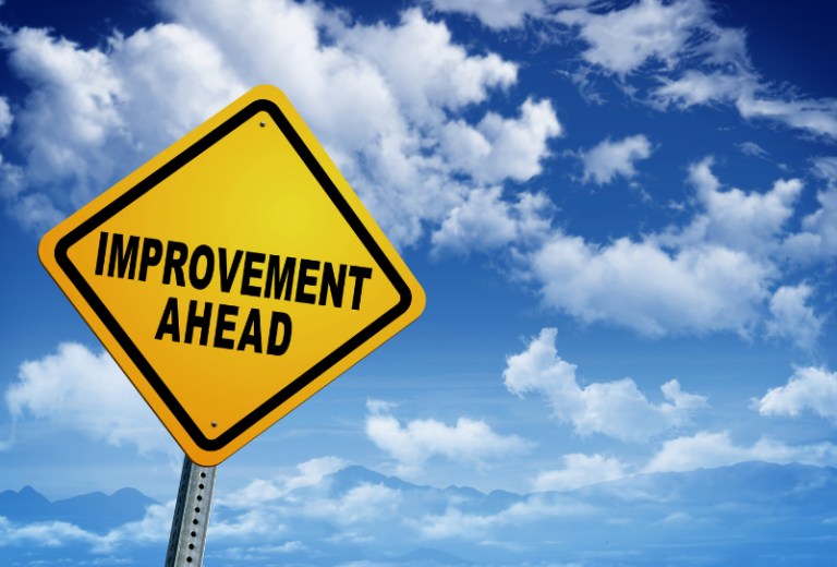 Yellow road sign with Improvement ahead written on it against a cloudy blue sky