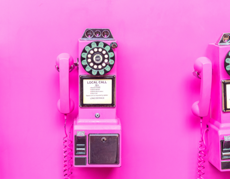 old rotary phone fixed to a wall on a bright pink background